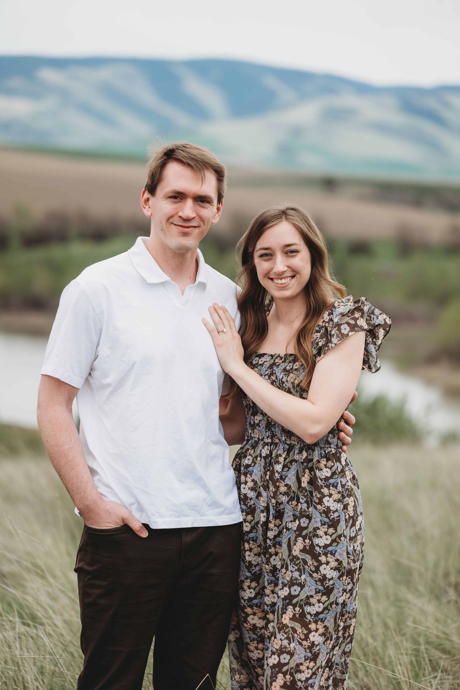 A newly engaged couple looking at the camera smiling with the Blue Mountains in the background.