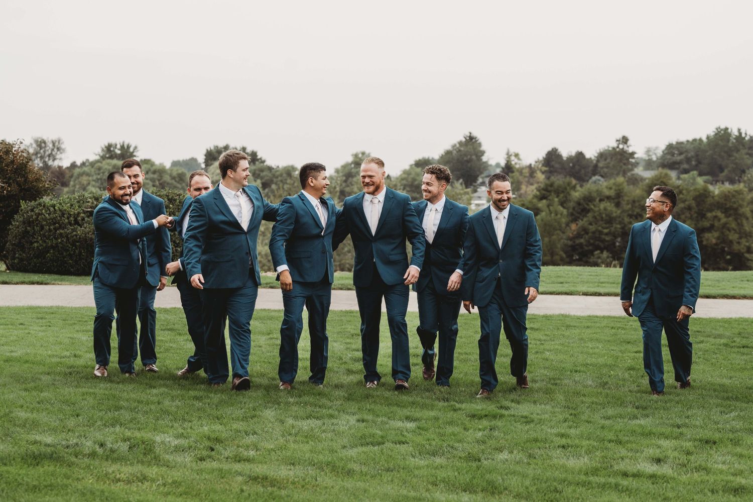 A groom and his groomsmen walking through a grassy field and laughing together.