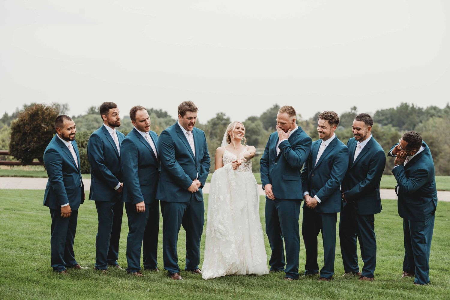 A bride surrounded by groomsmen showing off her wedding ring