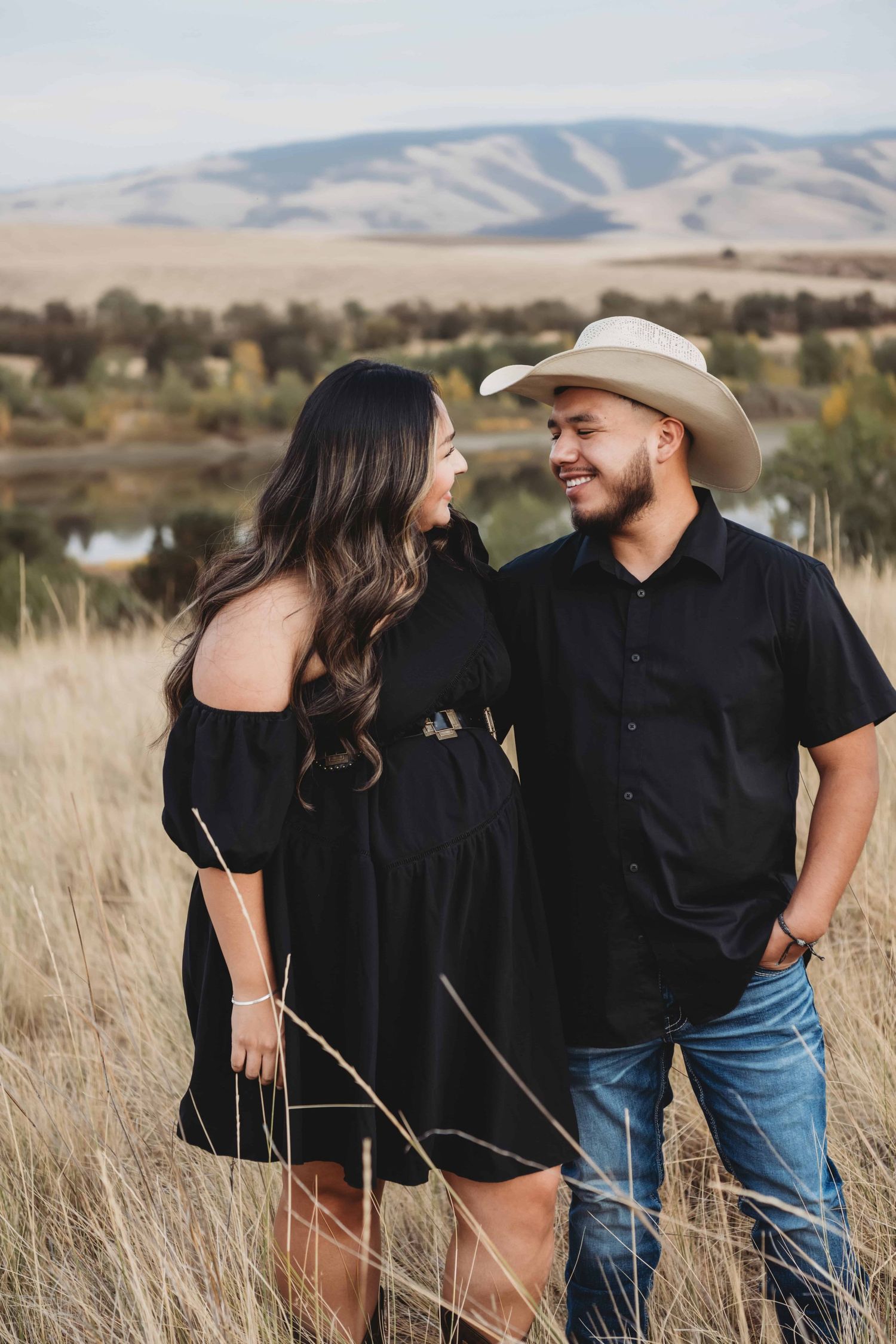Couple smiling at each other during an outdoor couples session in the rolling hills outside of Walla Walla, Washington.