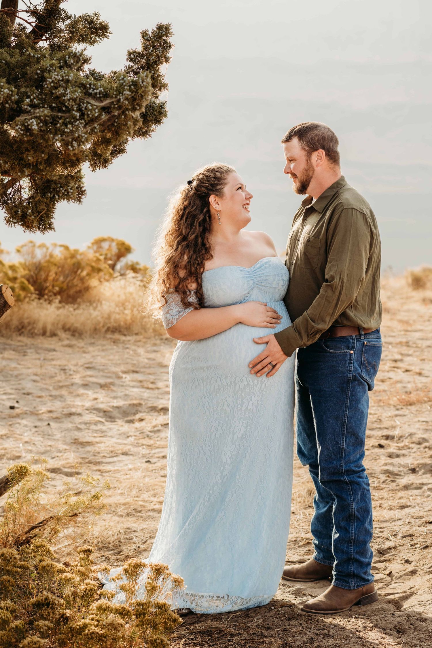 A portrait of an expecting couple looking at each other and laughing with a hand on the baby bump.