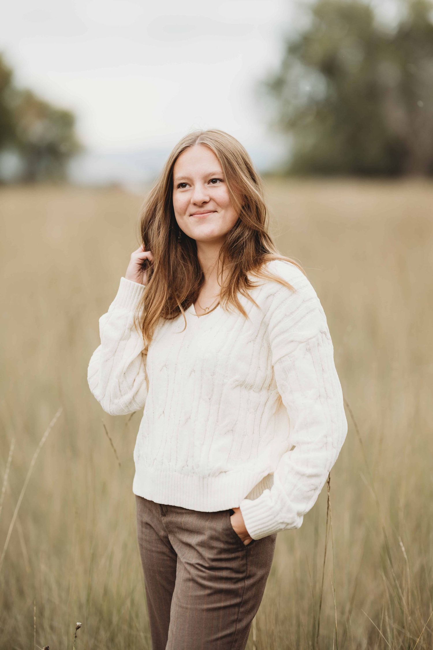 A high school senior wearing a cream sweater looking off into the distance with a soft smile on her face.