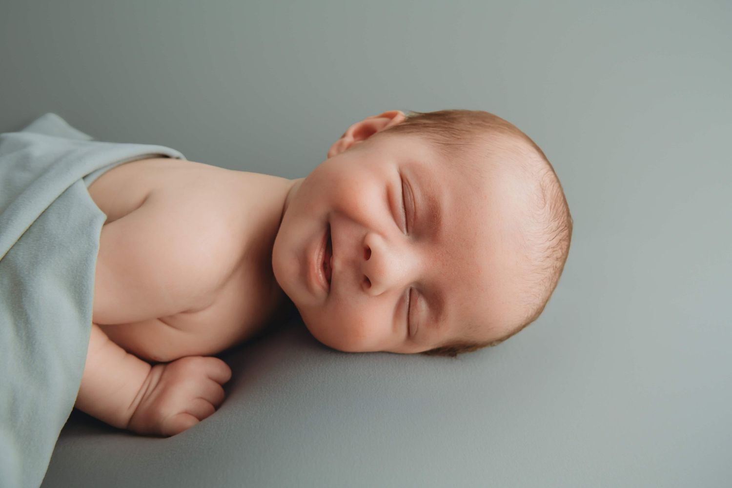 A newborn baby laying on a light blue blanket and smiling.
