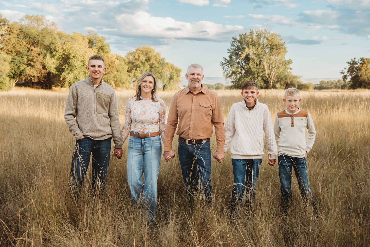 A family with three boys standing together holding hands and smiling for the camera.