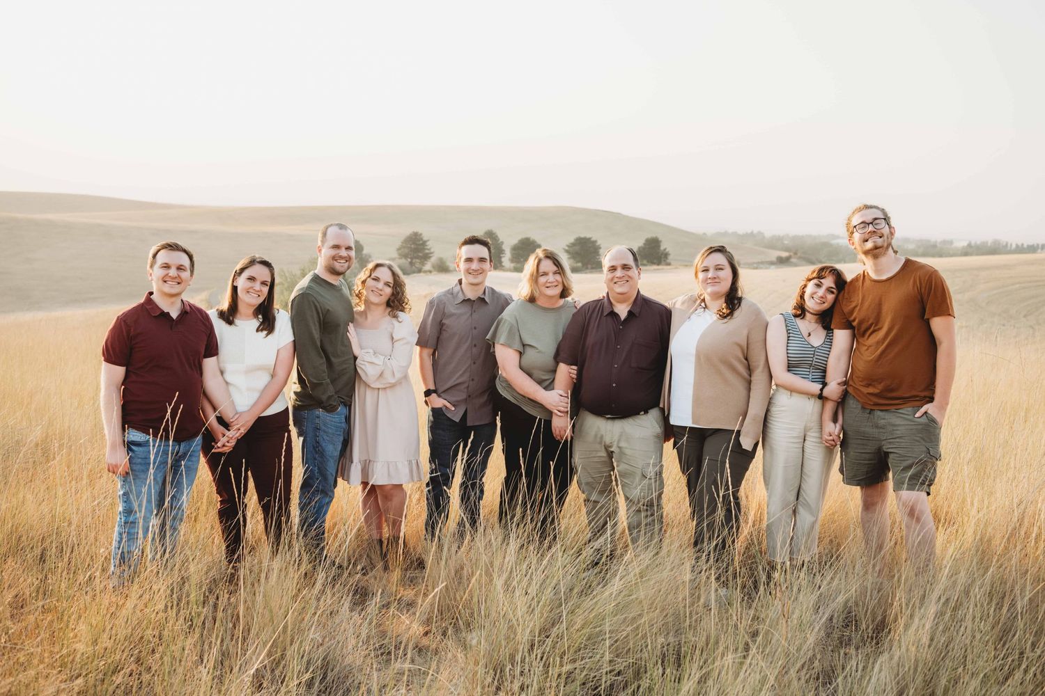 An extended family portrait of a family of ten standing in a golden field with rolling hills in the background.