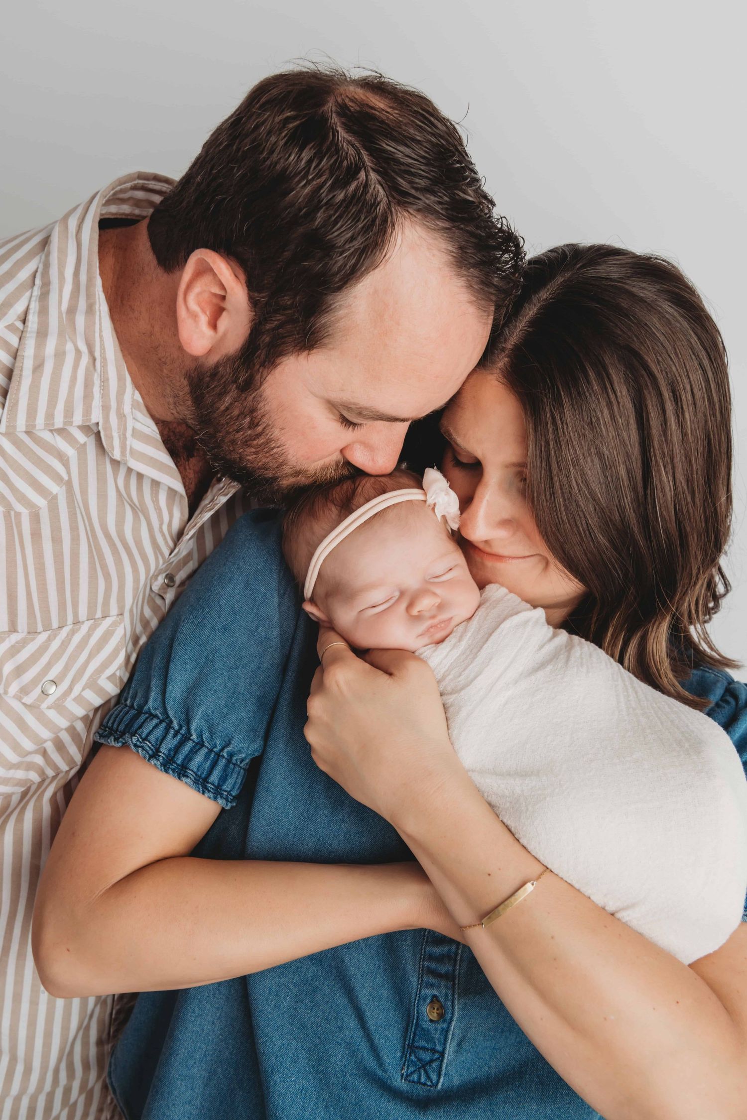 A timeless portrait of parents kissing their newborn's head.