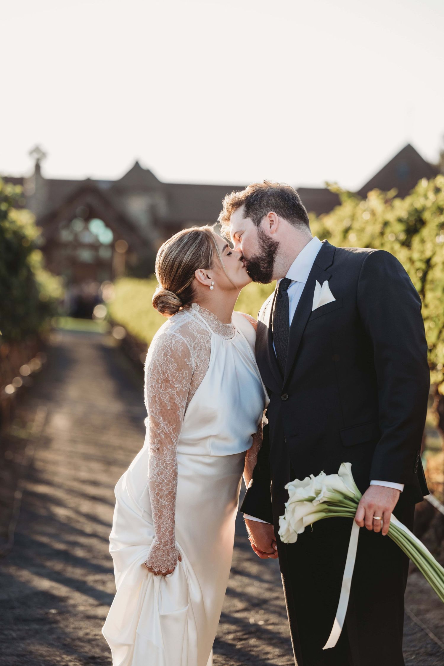 A couple kissing in a vineyard with a resort lodge in the background.