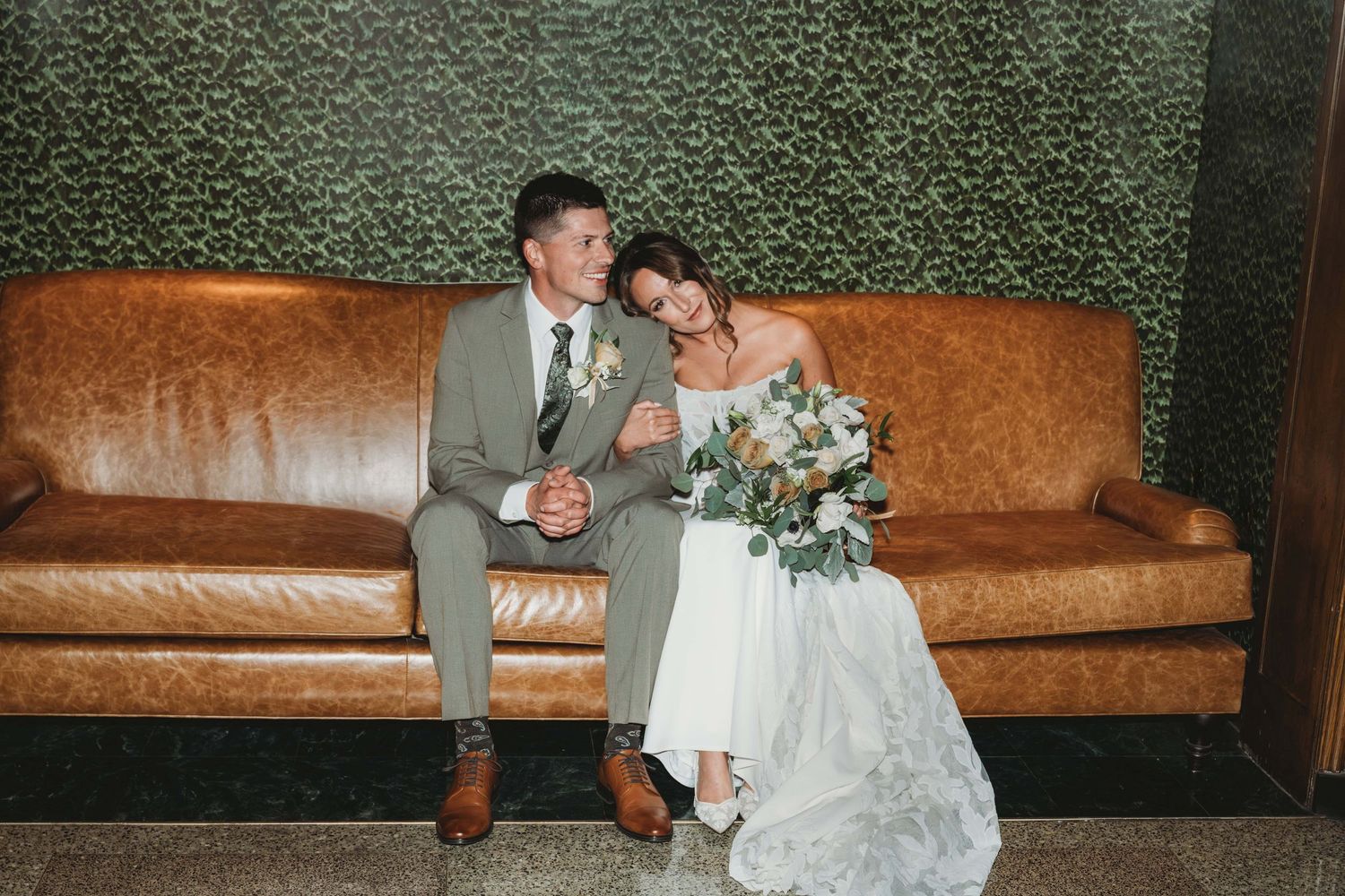A bride and groom sitting on a brown leather couch at the Marcus Whitman in Walla Walla.