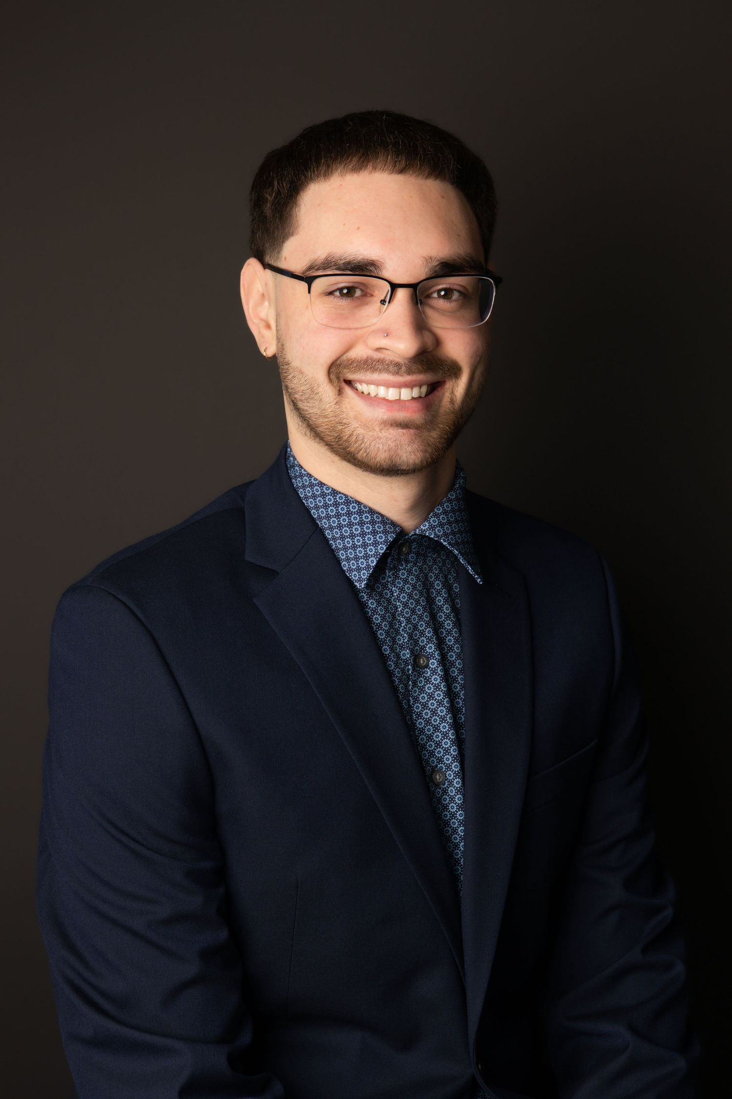 A man wearing glasses sitting for a headshot on a black background.