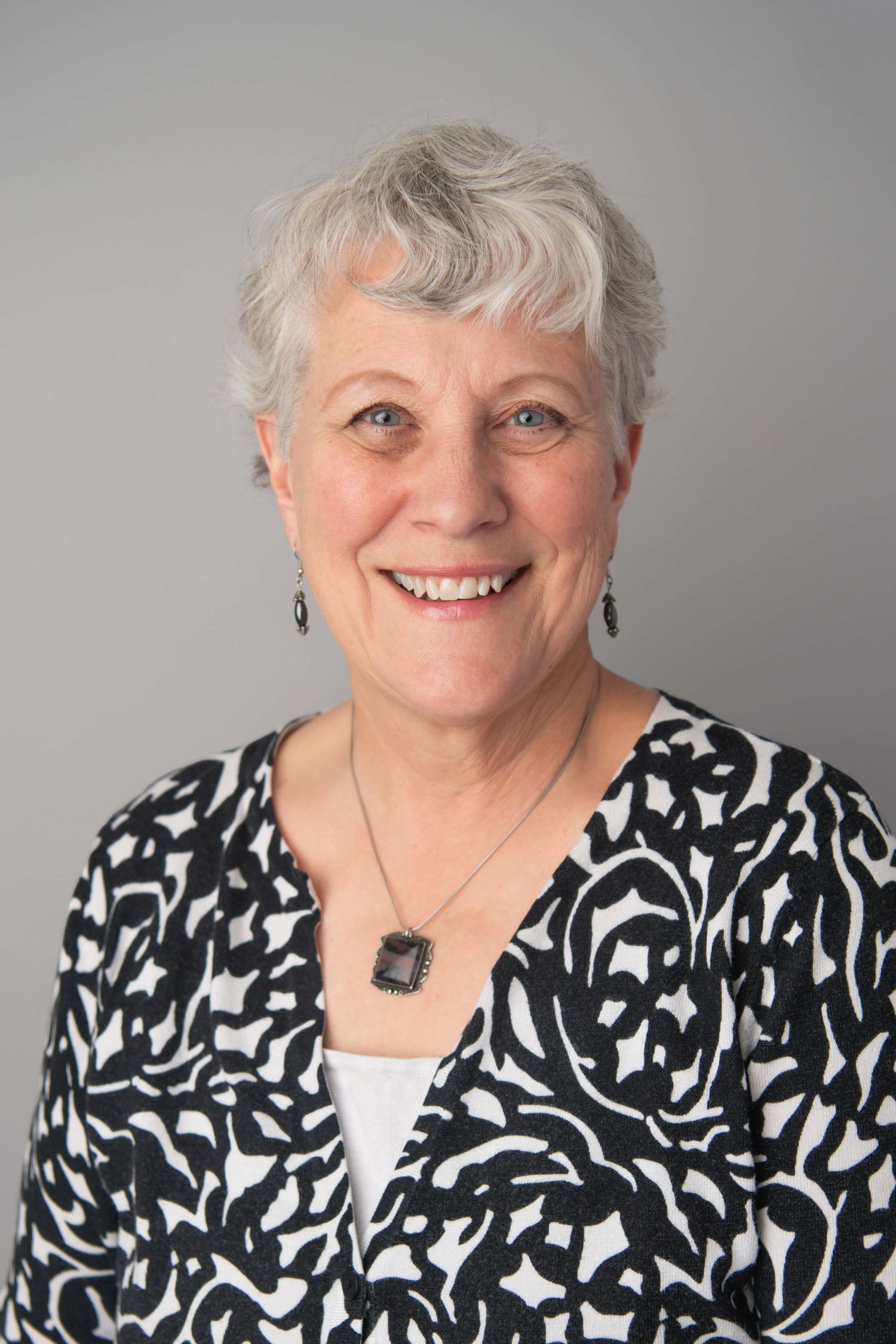 A classic headshot of a woman wearing a black and white blouse on a gray backdrop.