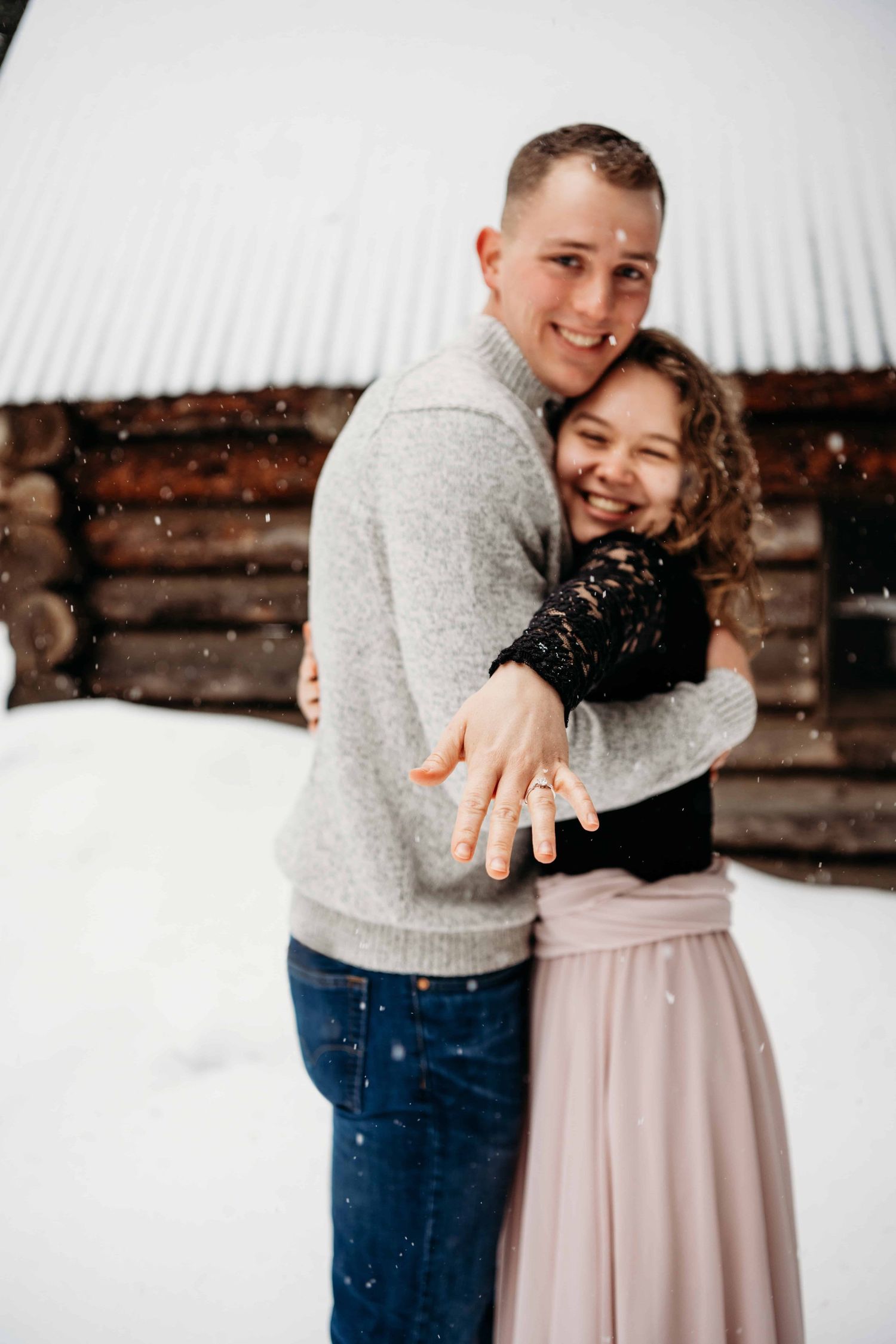 A woman holding her ring out while her fiancé hugs her.