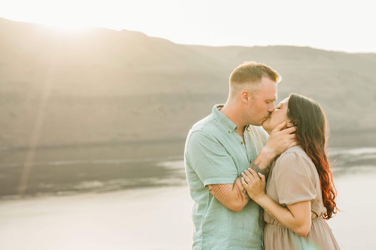 A couple kissing during golden hour with mountains in the background.
