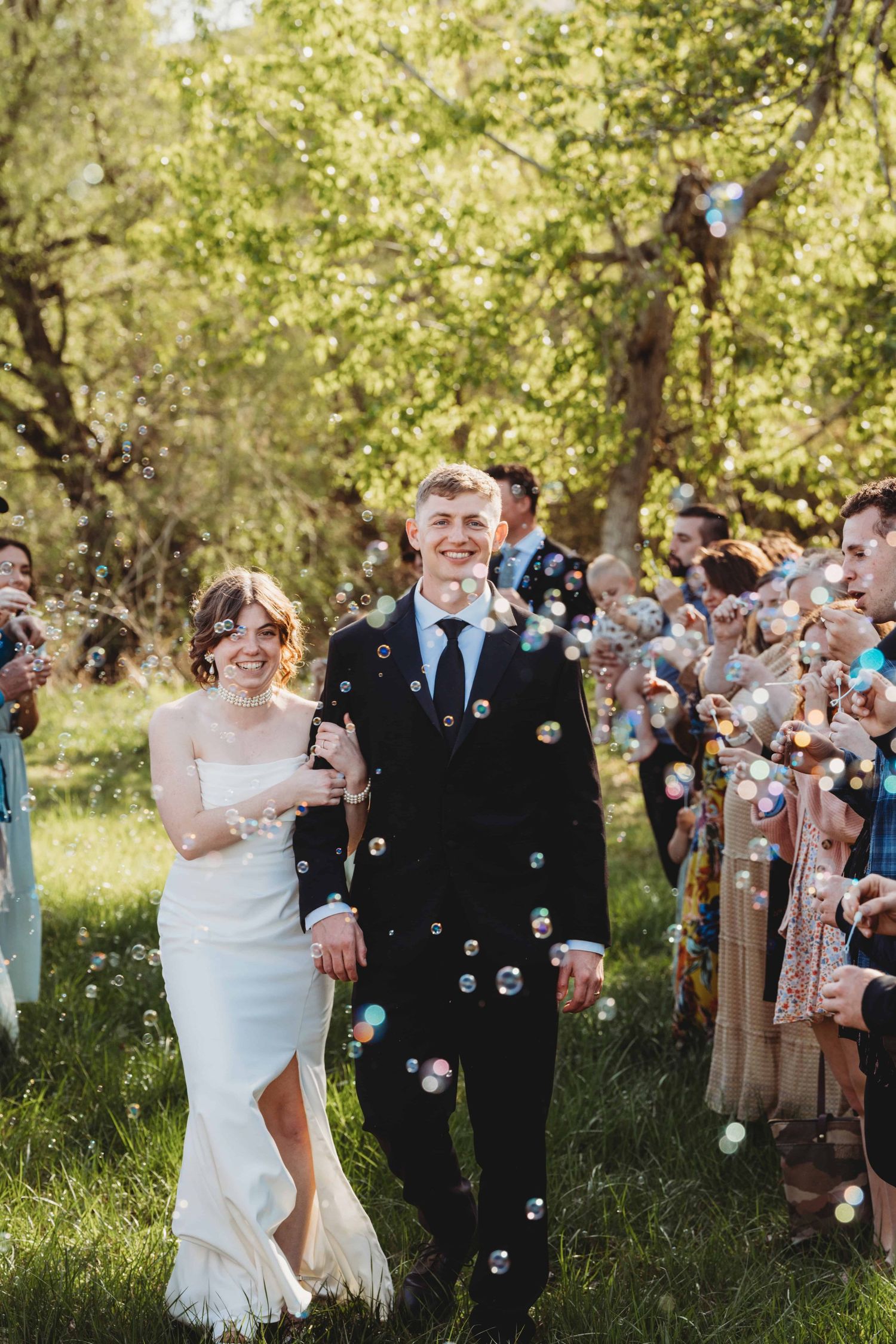 A bride and groom exiting their wedding reception with guests blowing bubbles at them.