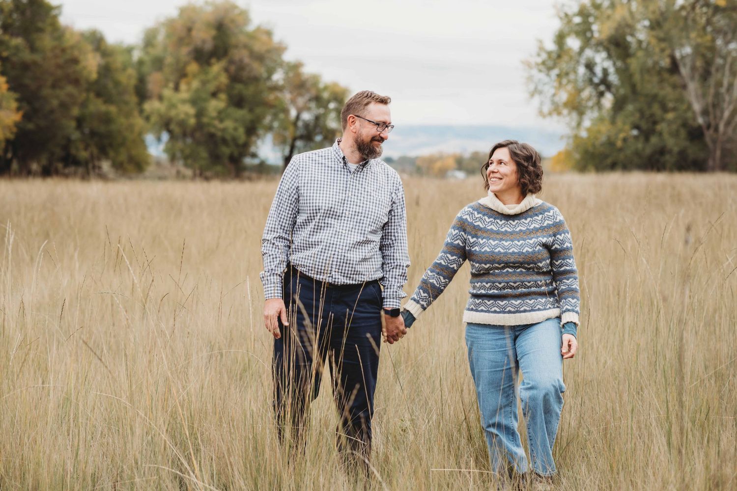 A couple holding hands walking while they look at each other and laugh.