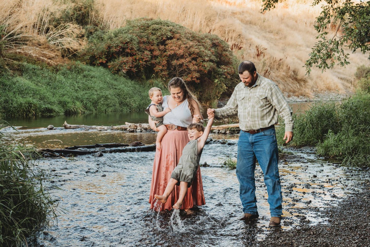 Outdoor family photography in Walla Walla showing parents and young children playing together in a shallow creek.