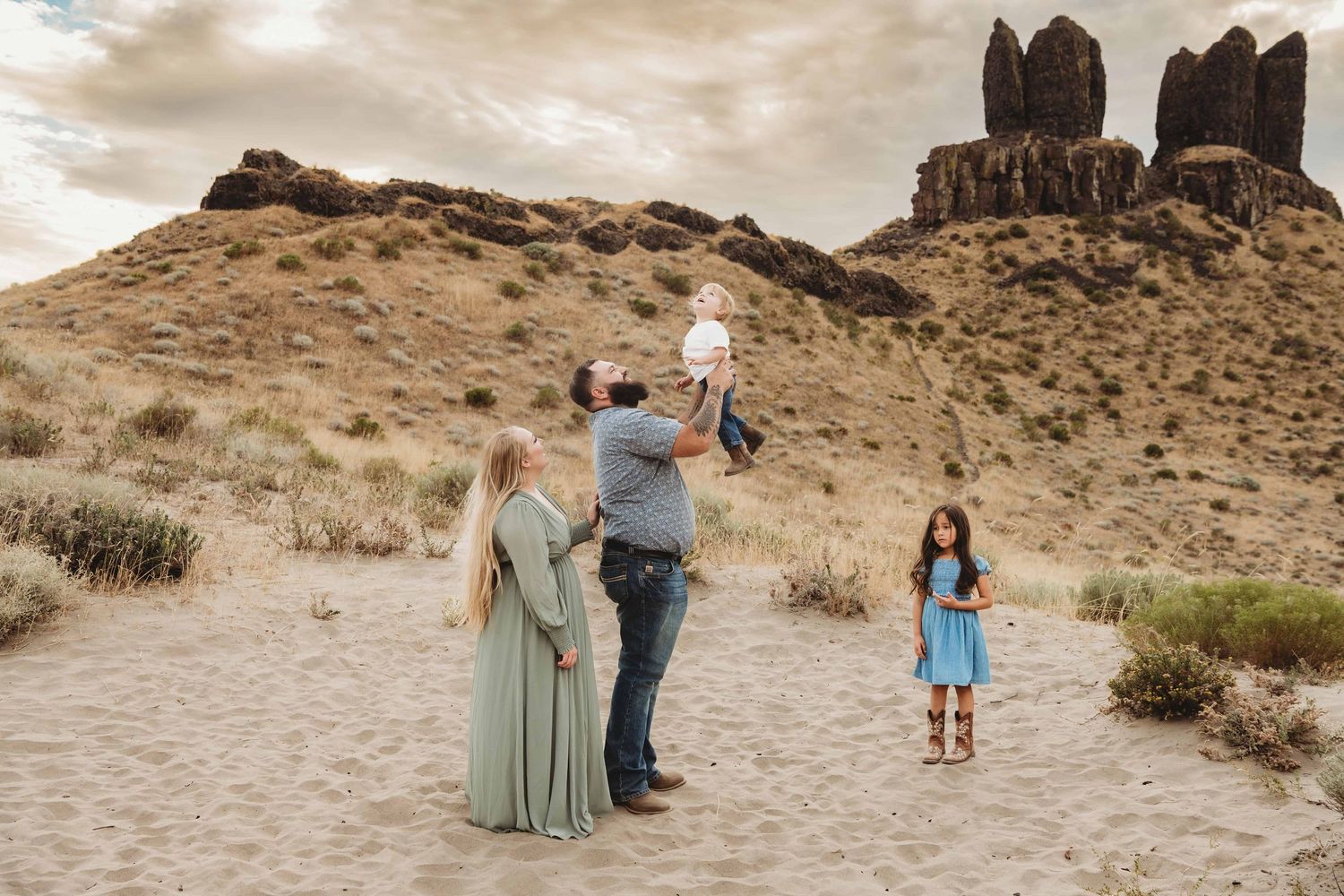 A candid family portrait of a father throwing his son in the air while the mother and daughter look on.