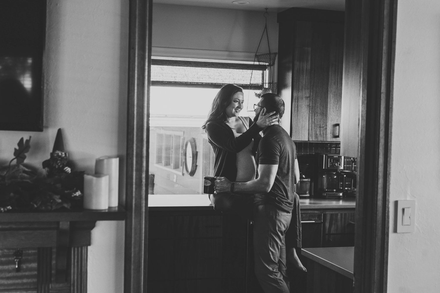 A pregnant woman sitting on her kitchen counter and laughing at her husband.