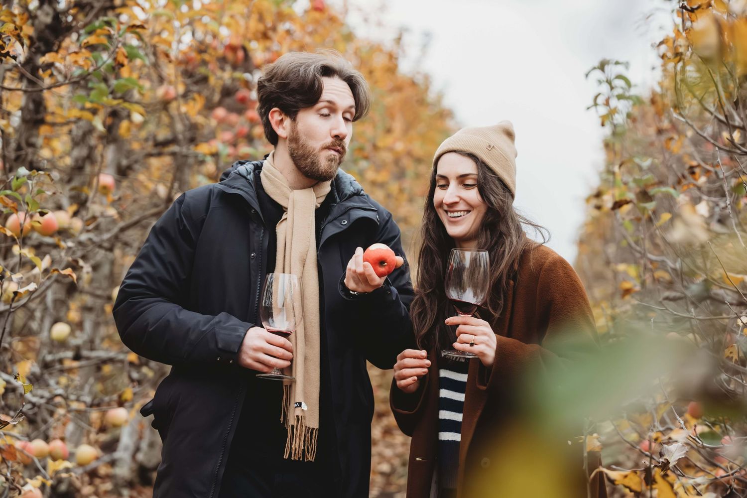 A man taking a bite of an apple that he just picked from a tree with his girlfriend standing next to him smiling.