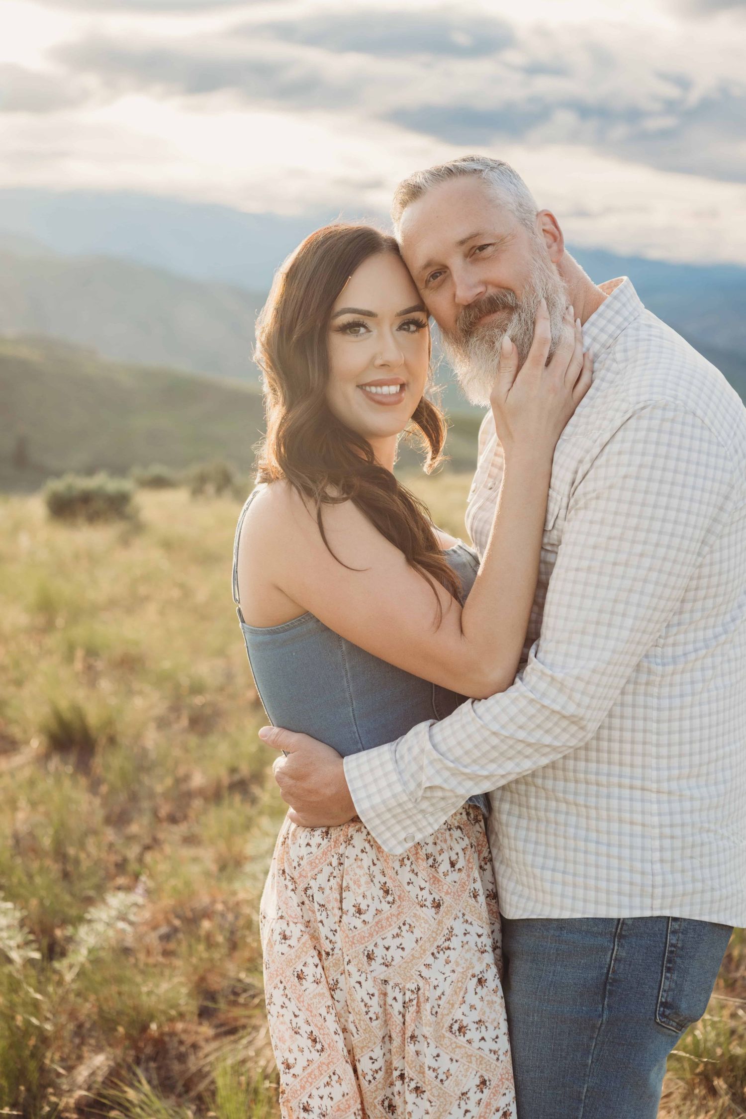 A couple looking at the camera and smiling with their faces close to each other.