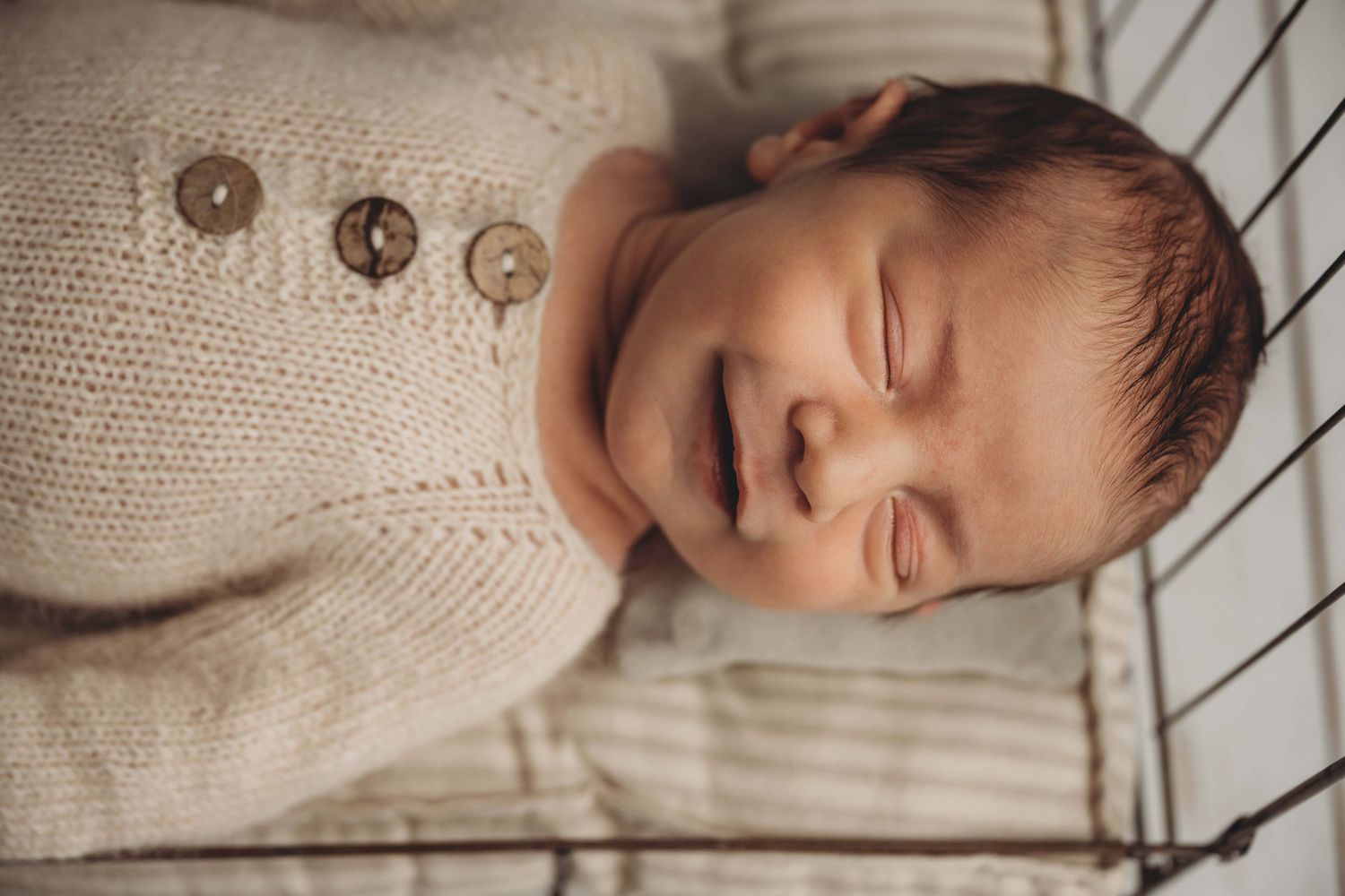 A newborn sleeping on a wire bed with a striped mattress and smiling.