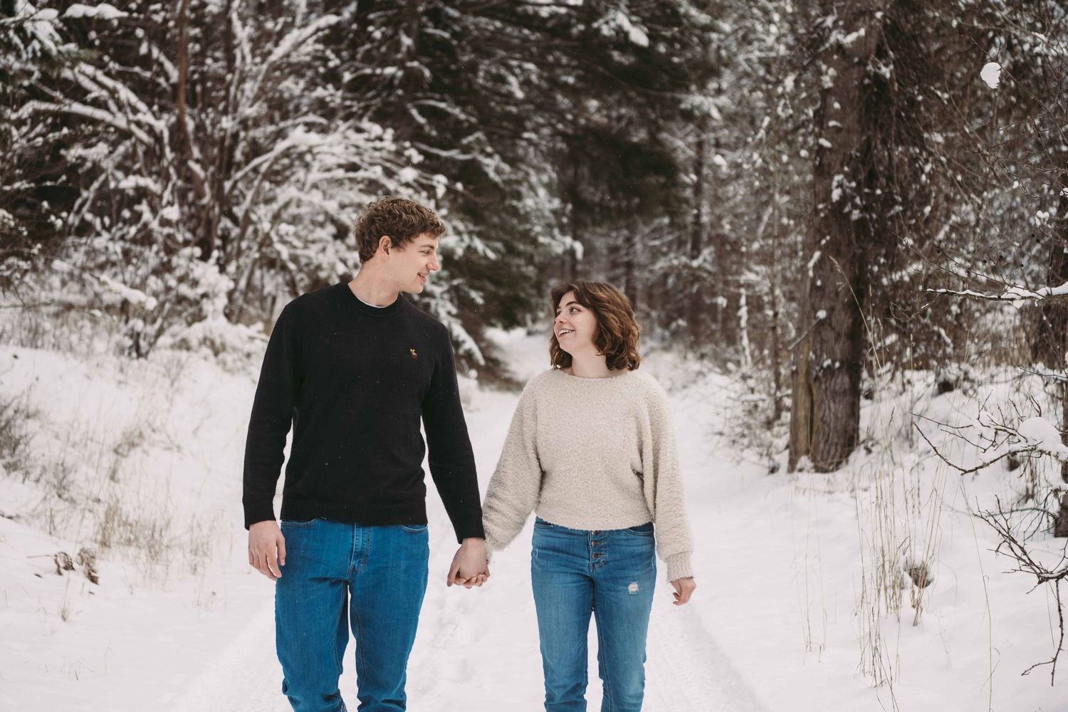 A couple walking through a snowy forest holding hands during an engagement photoshoot in Walla Walla.