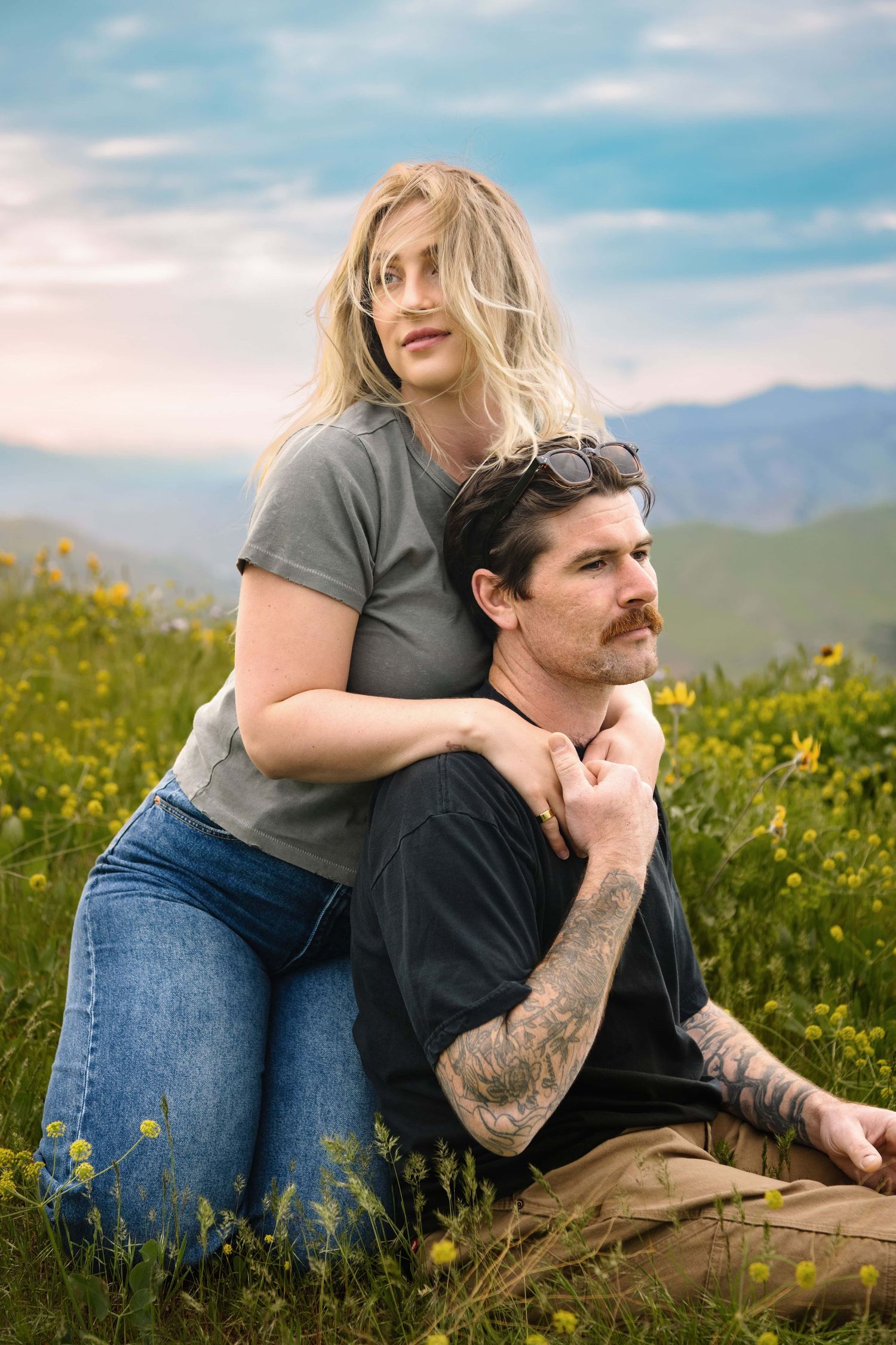 A couple sitting in a bed of wildflowers on a windy golden hour evening, with the wind blowing her hair, captured by a Chelan photographer.