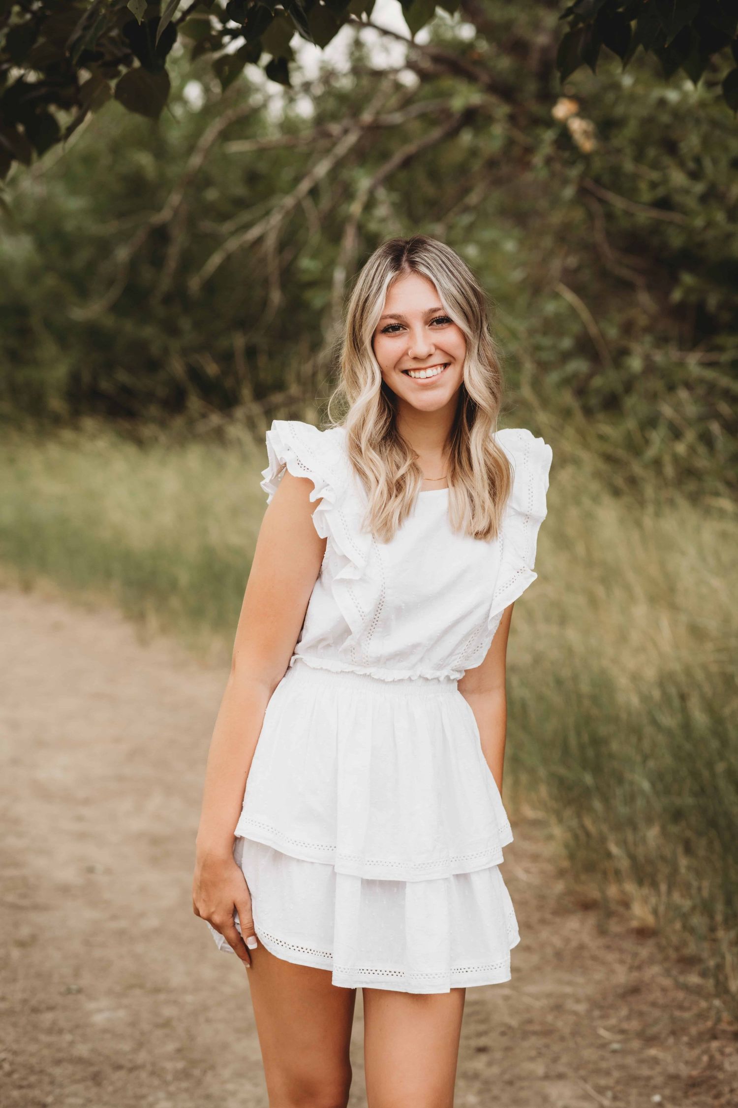 A girl in a white dress smiling for the camera during her senior photo session.