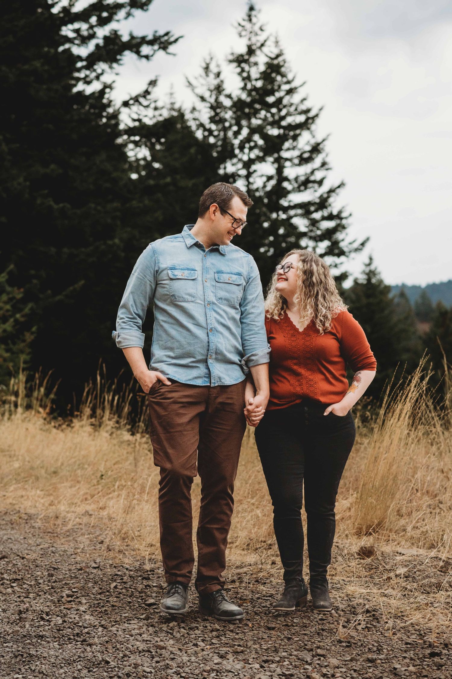 A couple standing holding hands and looking at each other in a mountainous area.