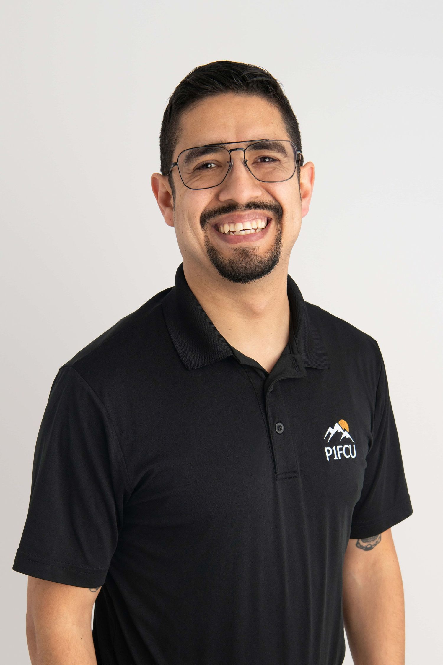 A professional headshot of a man wearing a p1fcu bank shirt on a white backdrop.