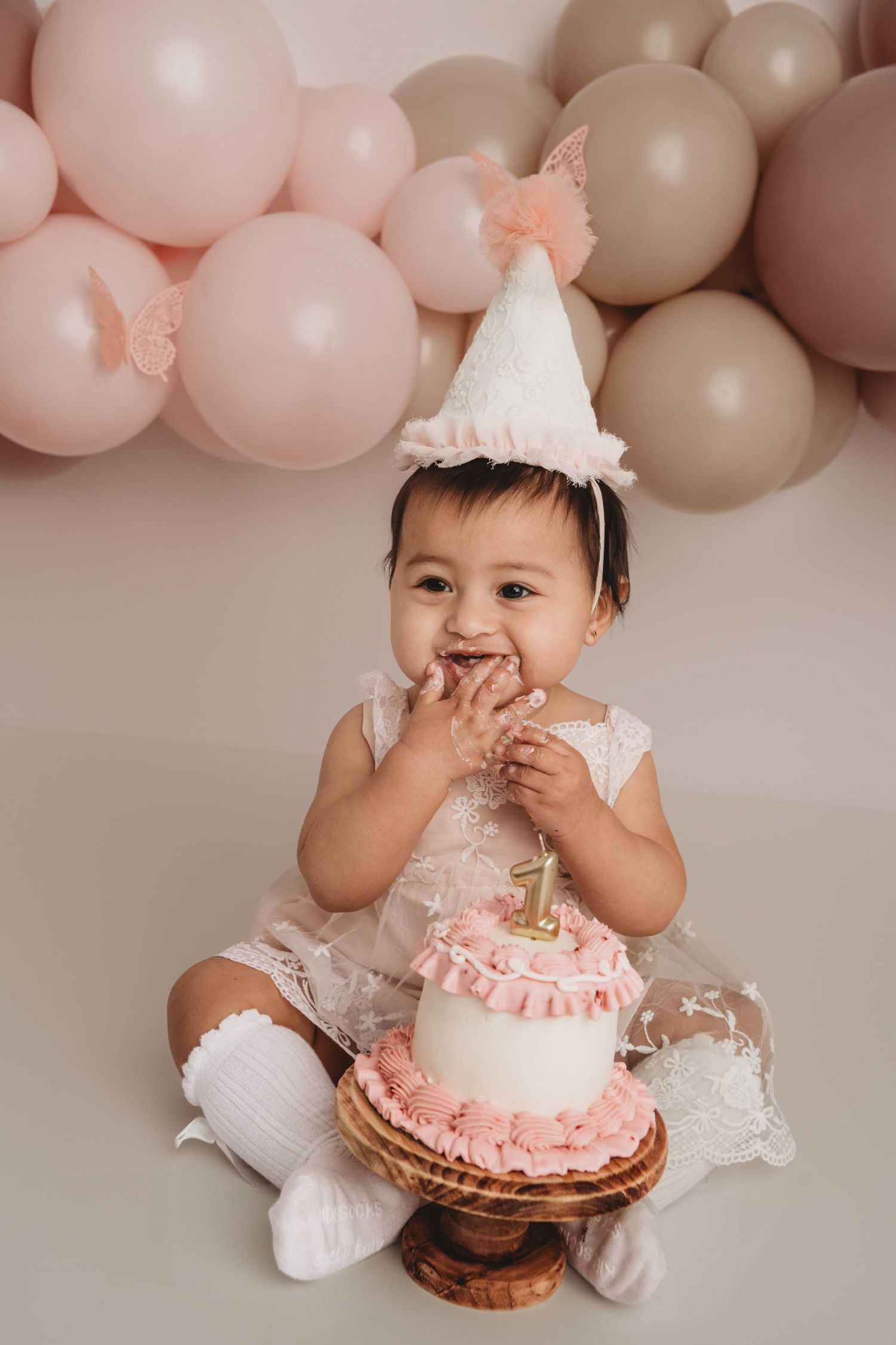 A Walla Walla photographer captures a one year old girl eating a pink and white cake and wearing a birthday hat.