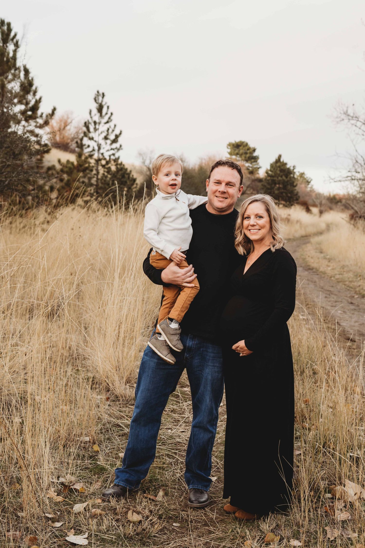 Walla Walla maternity photography session featuring expectant parents and their toddler standing together on a trail in a grassy field.