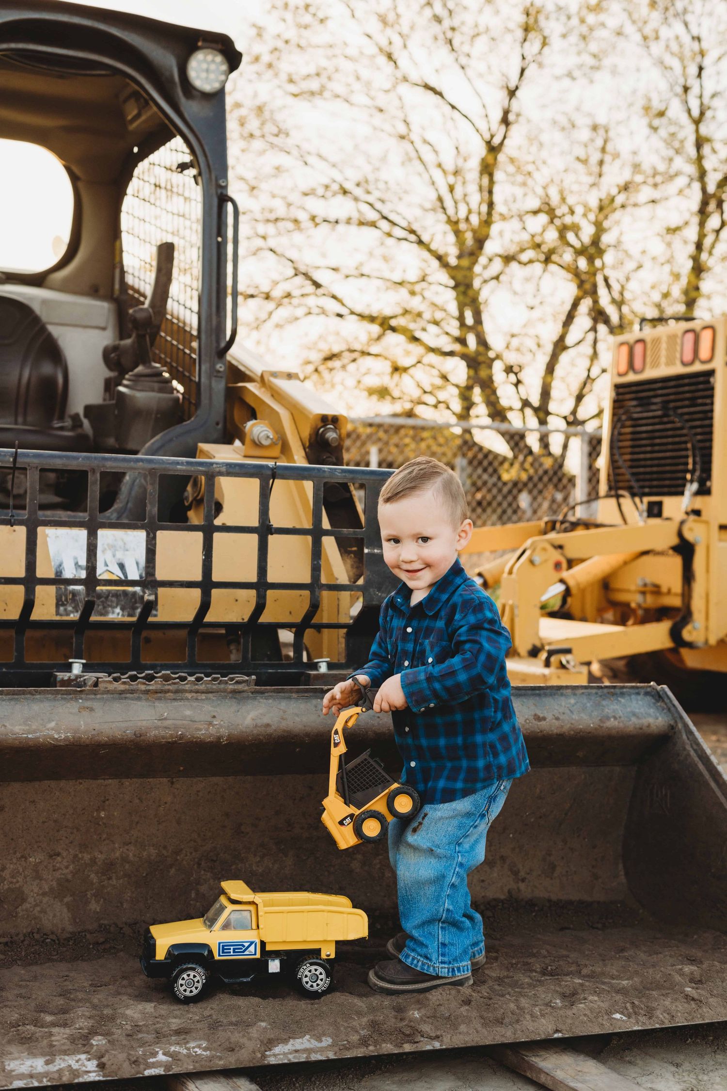 A two year old boy stands in a tractor and plays with his trucks in Walla Walla.