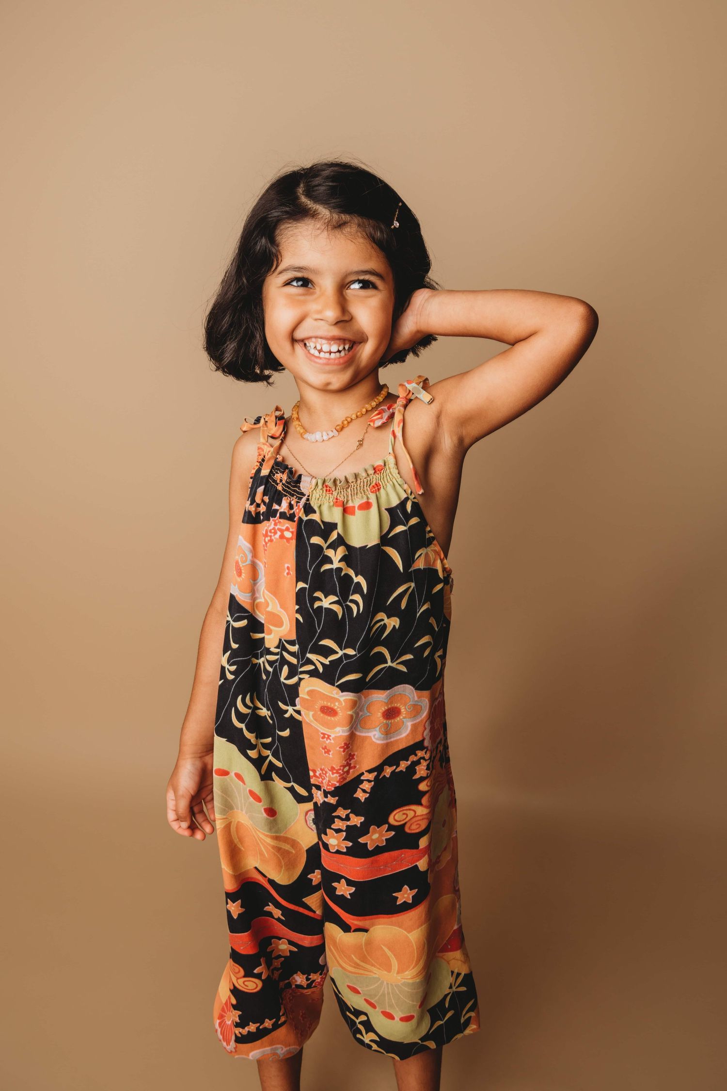 A girl dressed in a colorful jumper smiles on a brown backdrop at a Walla Walla portrait studio.