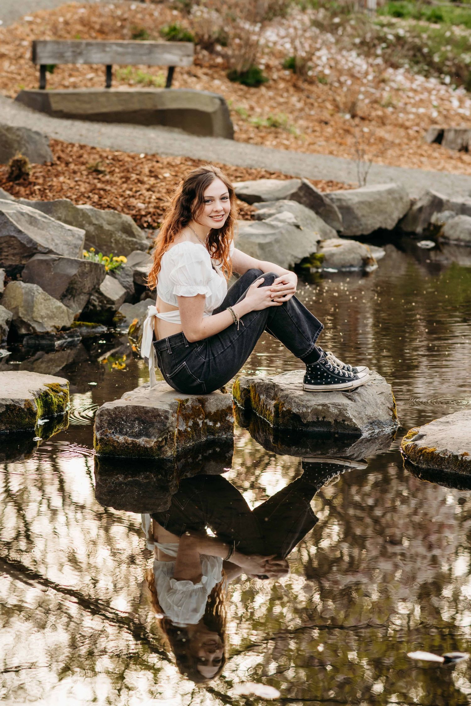 A senior sitting on a rock in the middle of a creek, with her reflection in the water in Walla Walla, Washington.