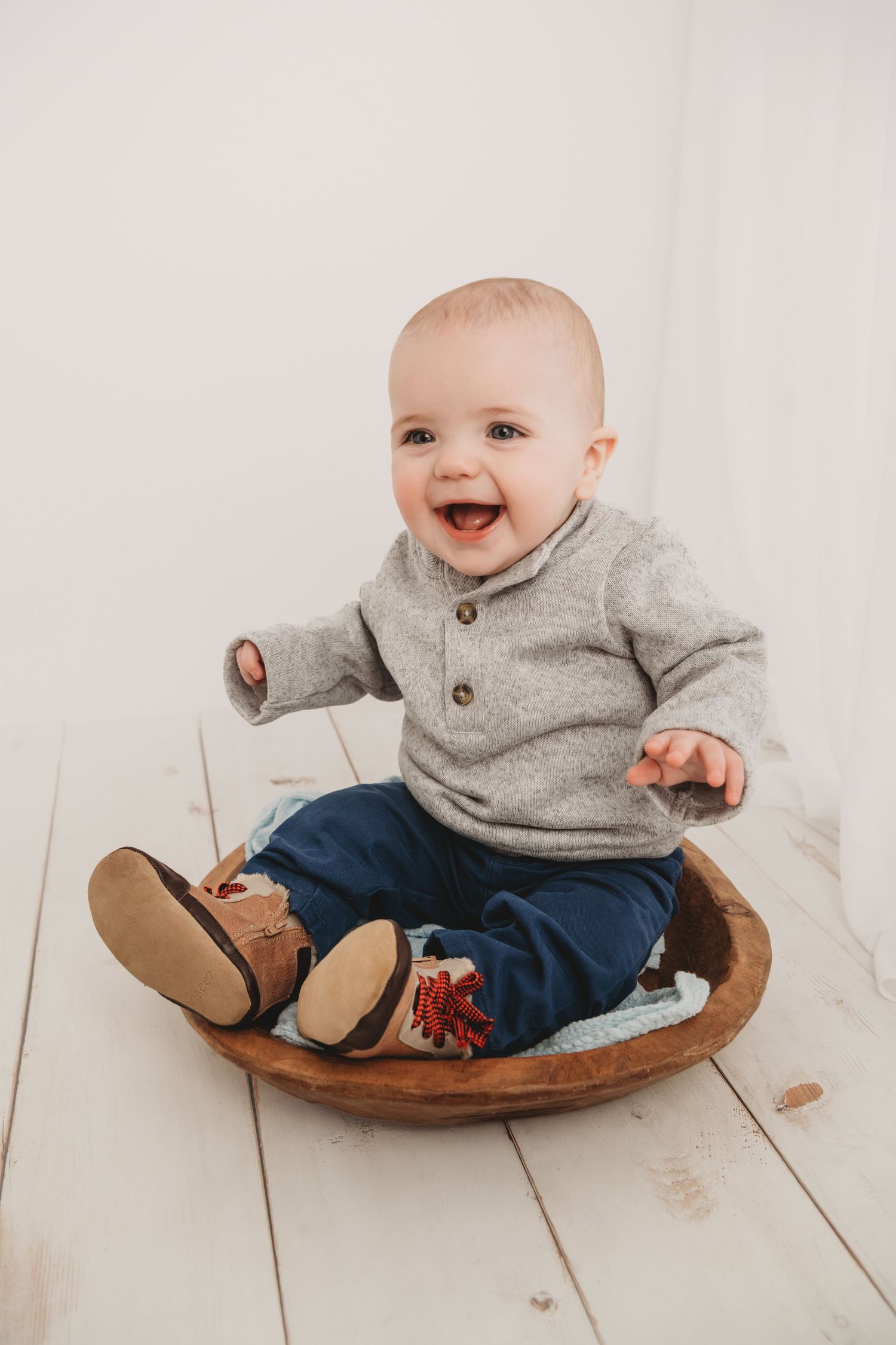 A baby baby sitting in a brown wooden bowl and laughing.