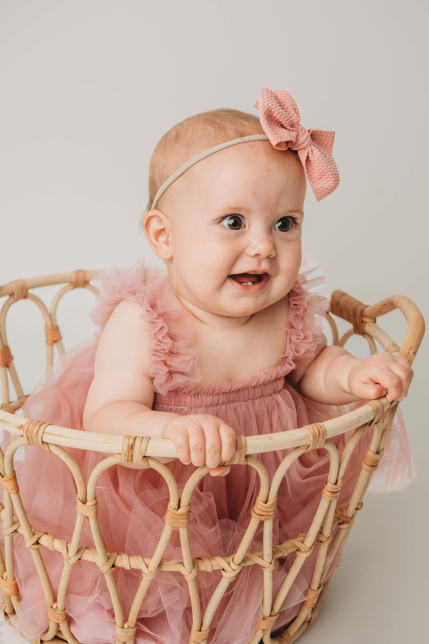A baby girl in a basket wearing a pink dress and bow.
