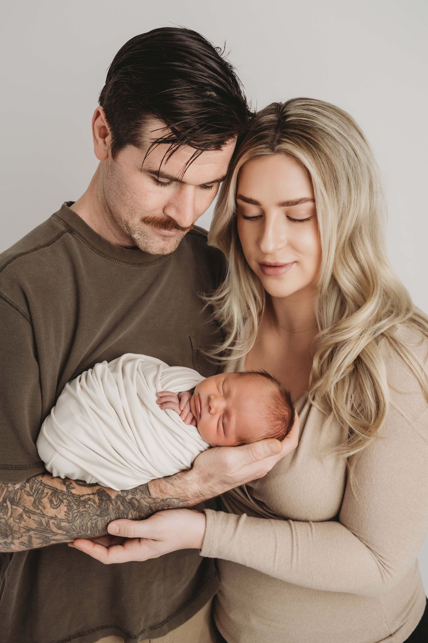 New parents look down and admire their sleeping newborn baby at a Tri-Cities newborn photography studio.