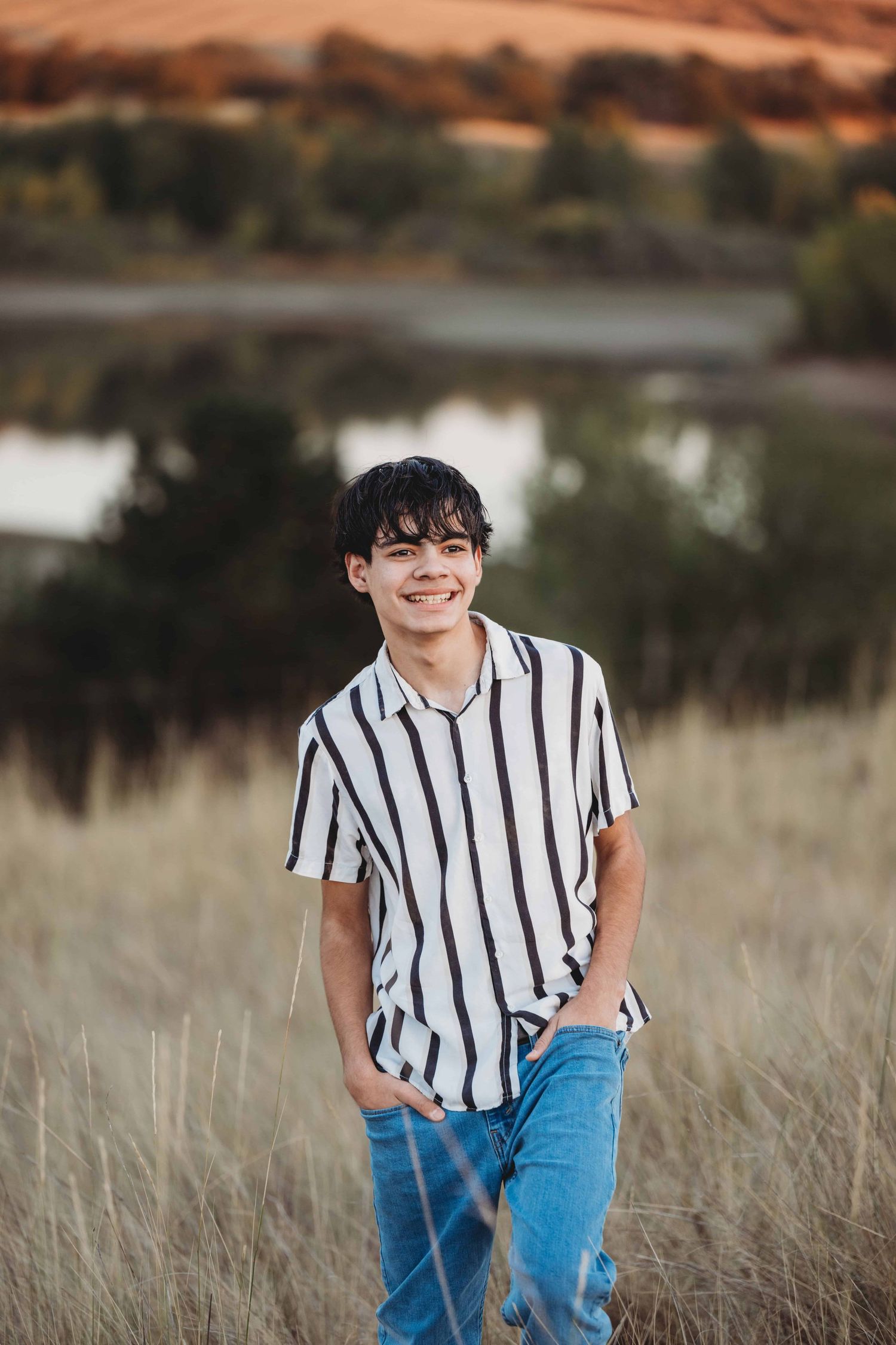 A candid portrait of a young man walking through a field with a lake in the background.