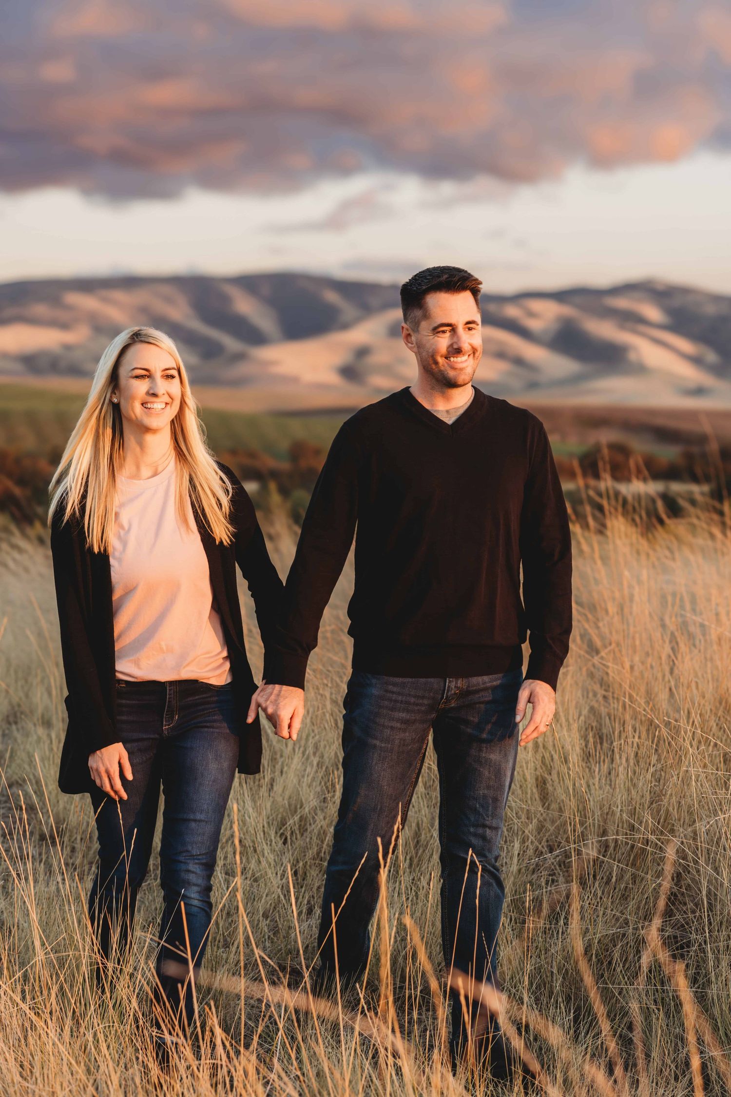 Couple holding hands and walking through rolling hills at sunset during a Walla Walla engagement session.