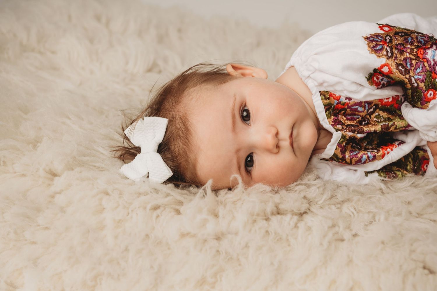 A baby girl laying on a soft cream flokati with a serious expression on her face.