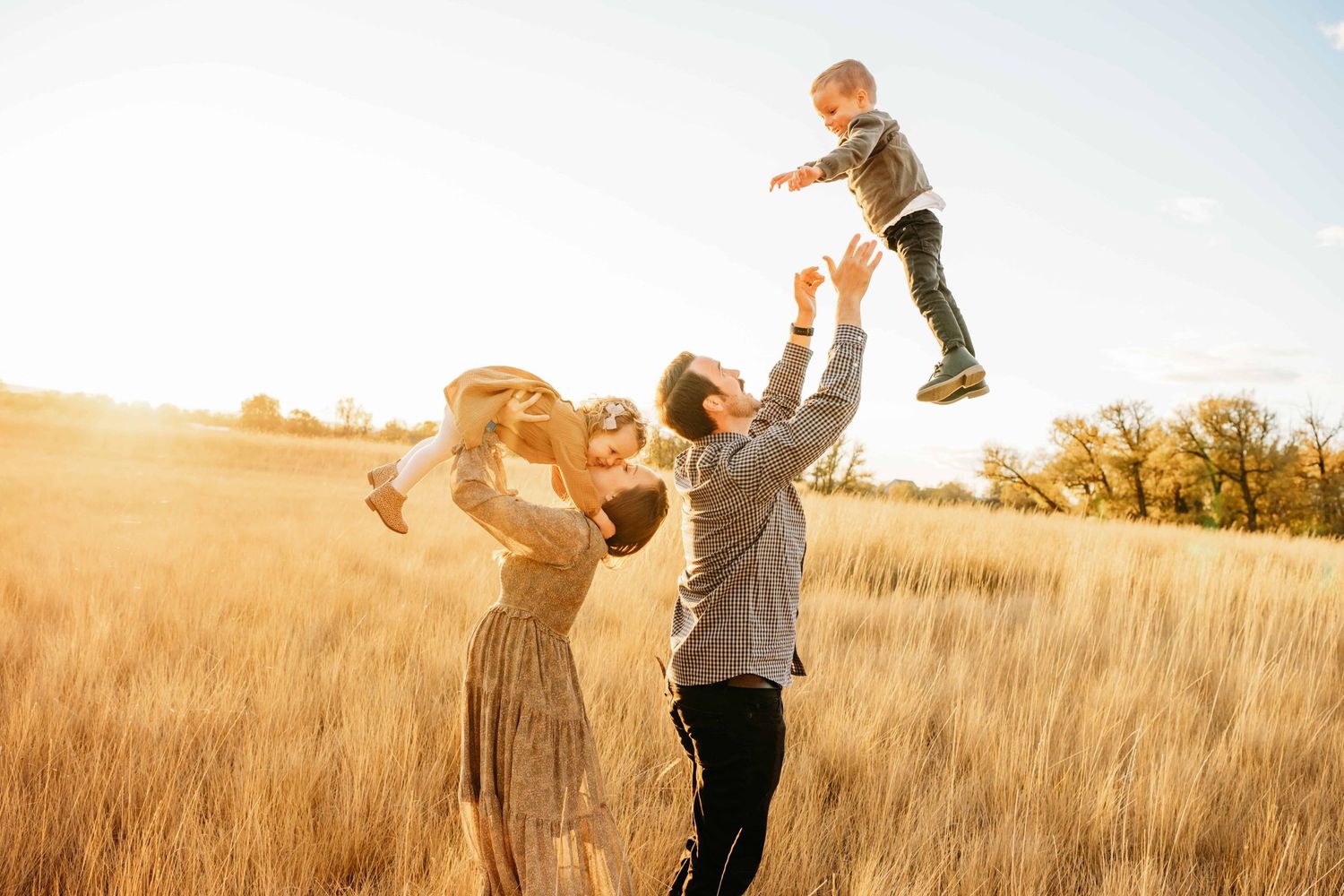 A Walla Walla photographer captures a candid family of four in beautiful golden hour lighting while the dad throws his son up in the air.