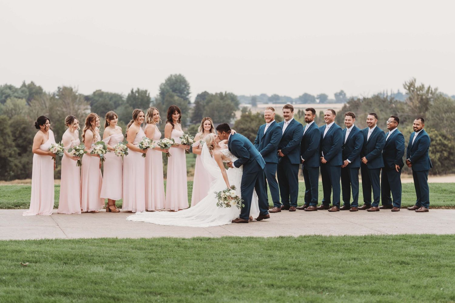 Bride and groom kissing in front of a large bridal party