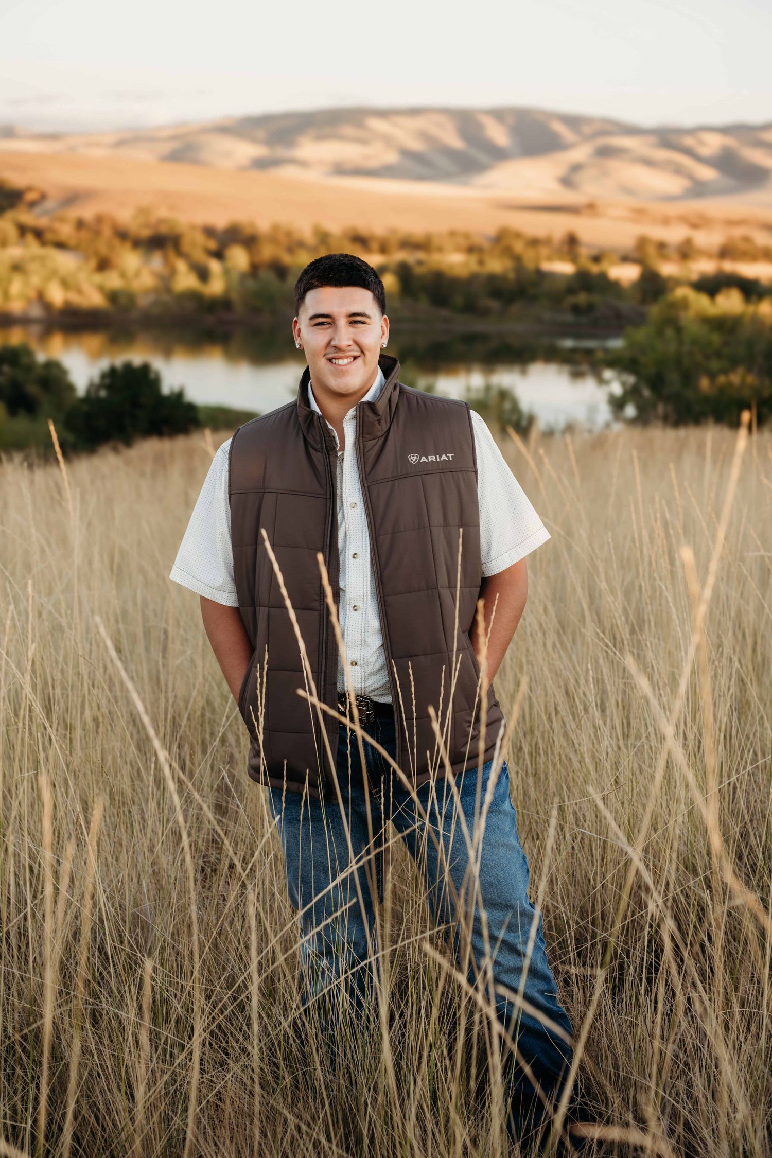A senior portrait of a young man standing in front of a lake and rolling hills in Walla Walla, Washington.