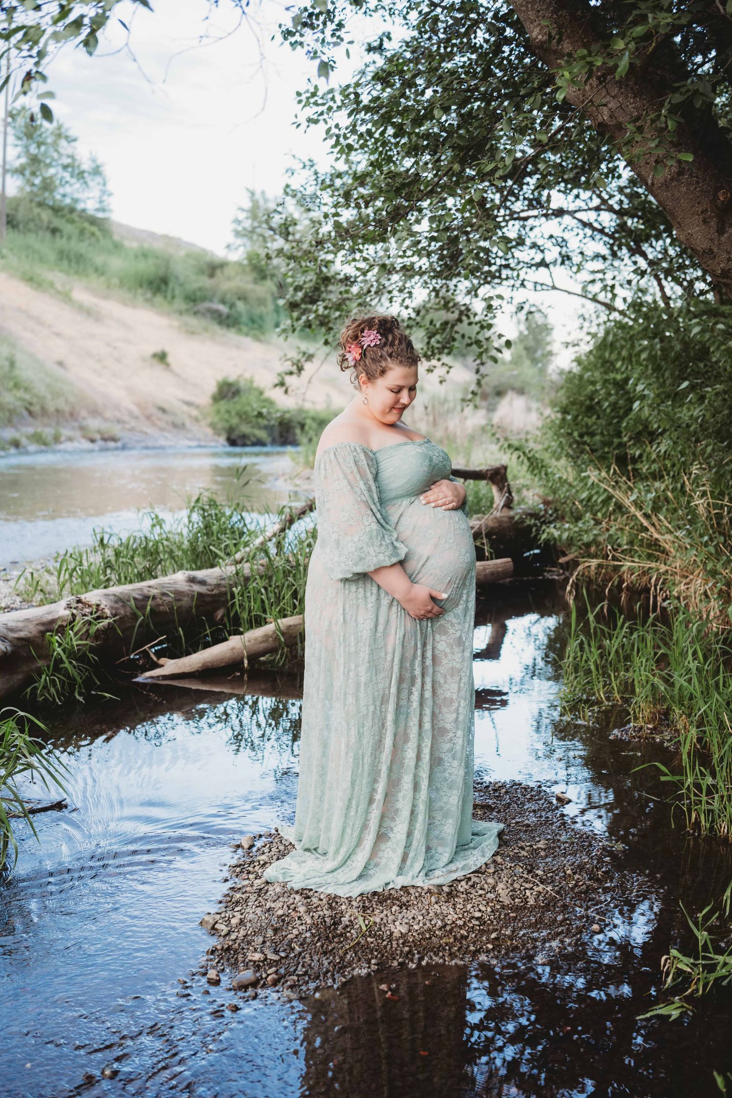 An expecting mother is captured looking down at her baby bump while standing in the middle of a creek in Walla Walla.