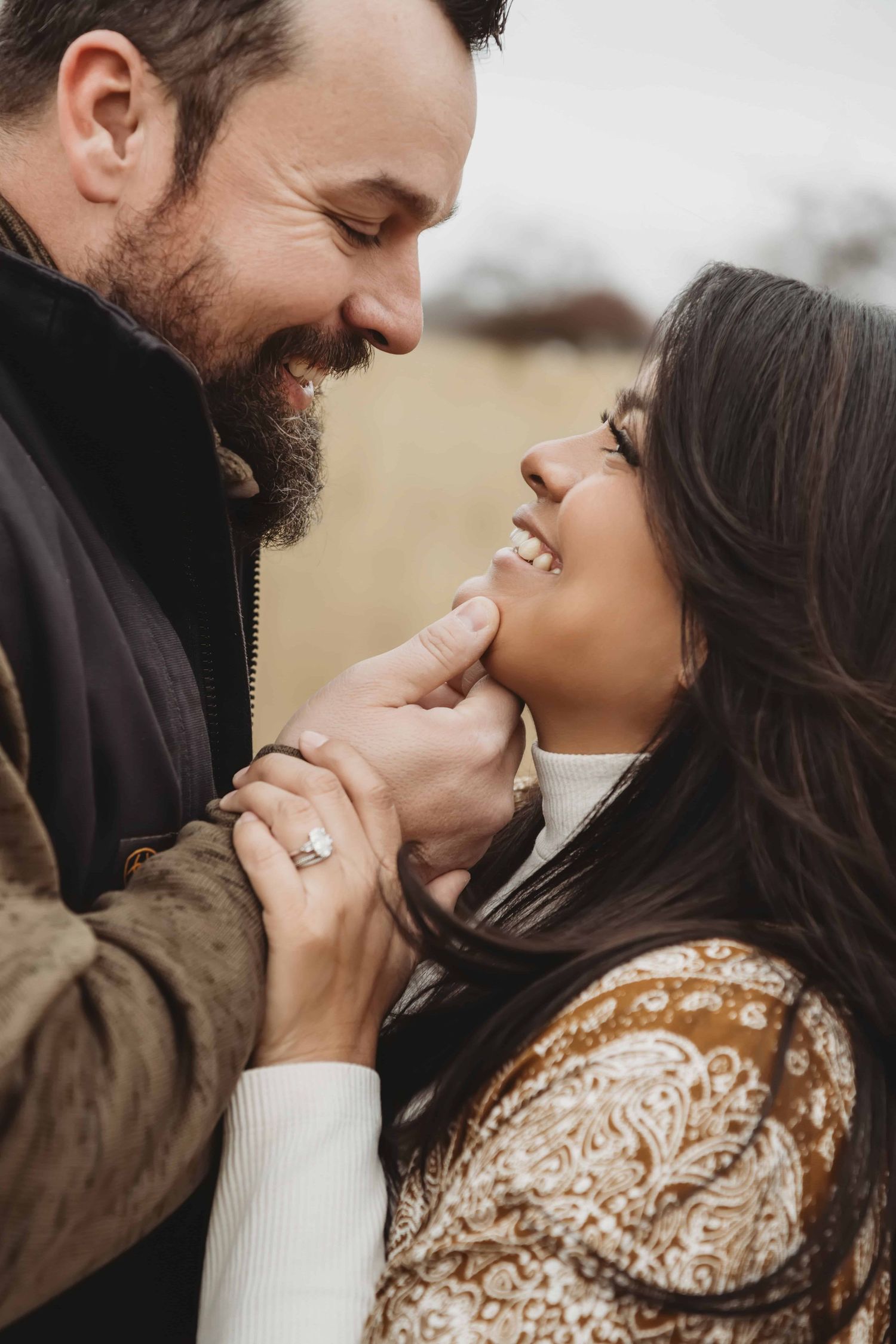A close up portrait of a man gently touching his wife's face as they smile at each other.