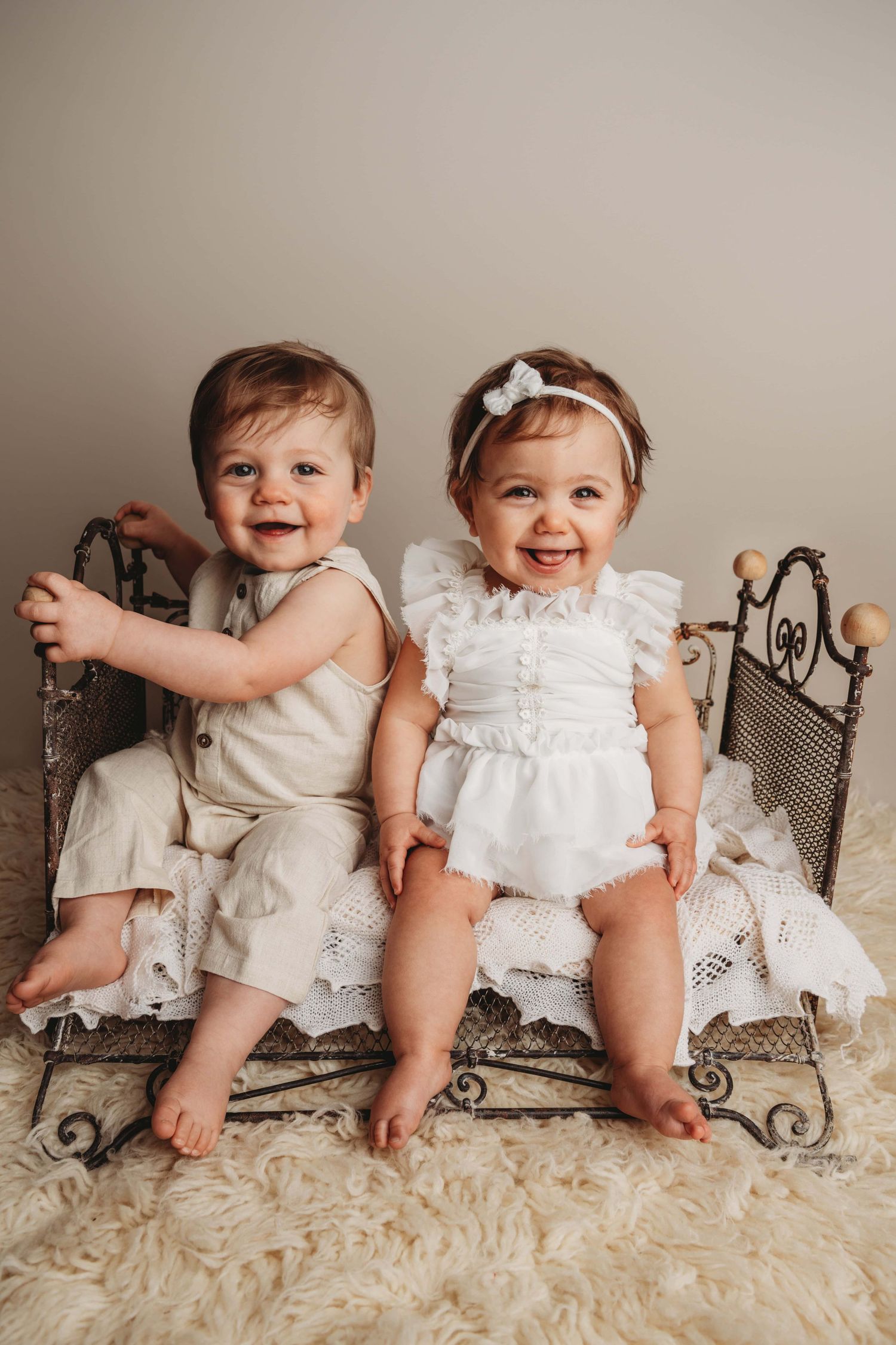A Walla Walla photographer captures twin one year olds sitting on a vintage bed on a soft cream flokati.