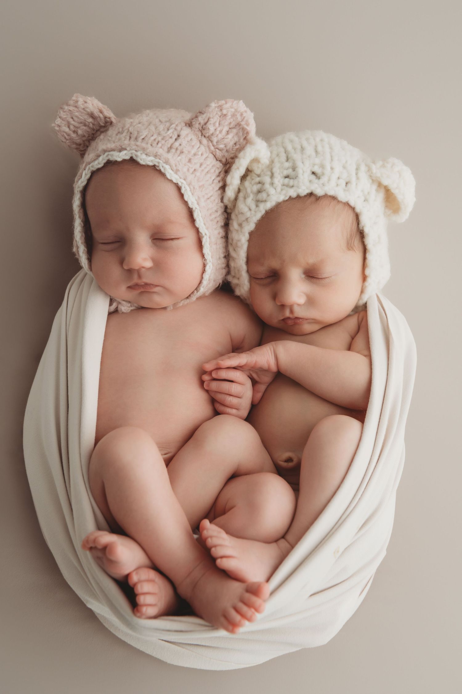 Twin newborn siblings born in Richland Washington sleeping while holding hands at a Walla Walla newborn studio.