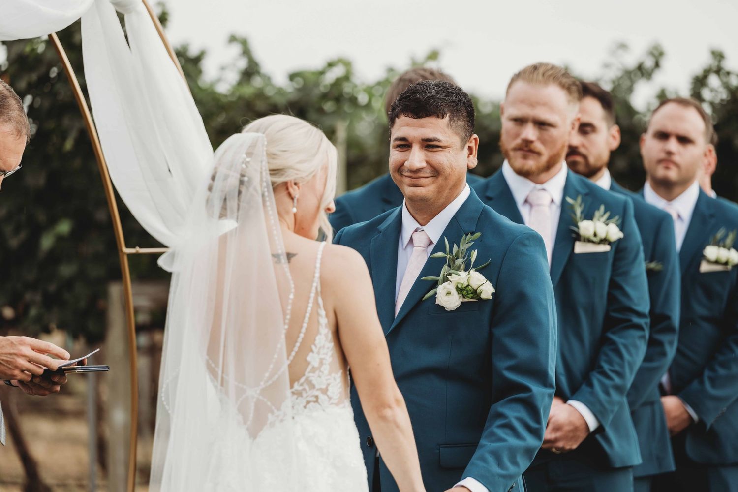 A groom looks at his bride and smiles at her during their wedding ceremony.