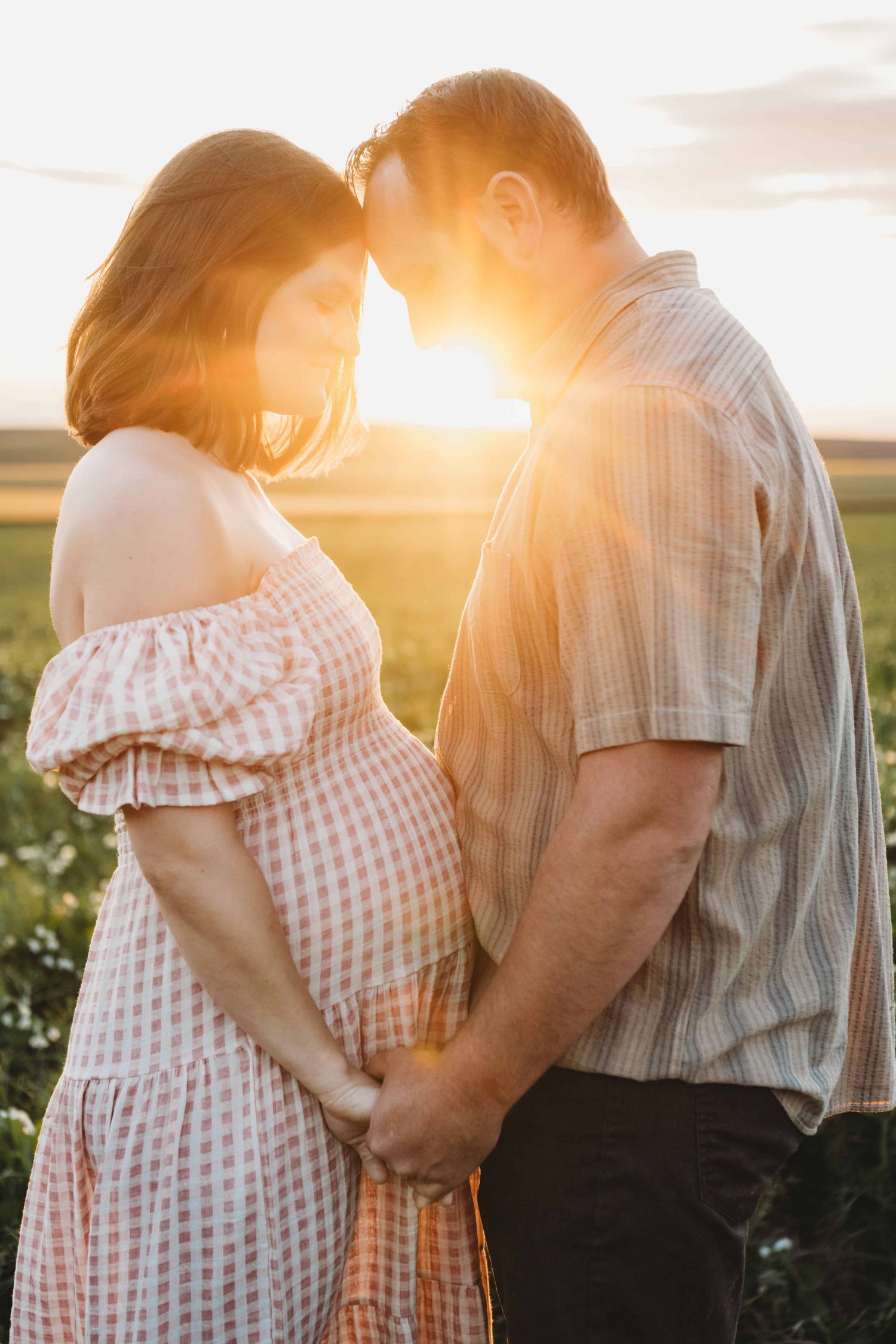 A couple shares an intimate moment with the golden sunlight shining in between them during a maternity photoshoot.