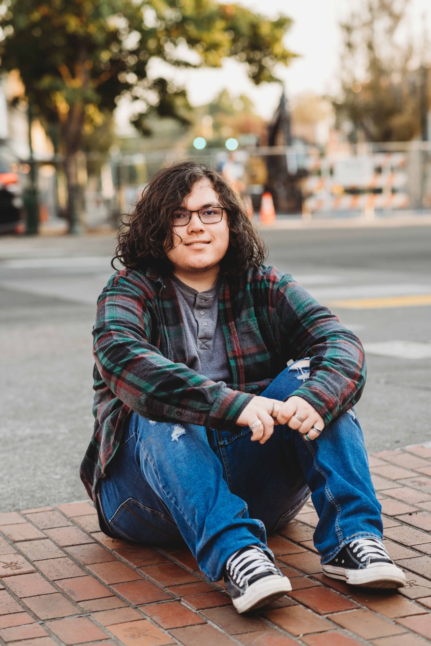 A senior portrait of a young man sitting on the ground in downtown Walla Walla, Washington with a soft smile on his face.